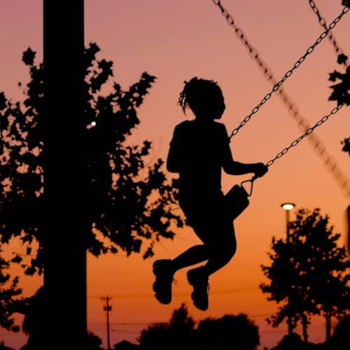 Photo d'une petite fille faisant de la balançoire, indistincte dans le soleil couchant