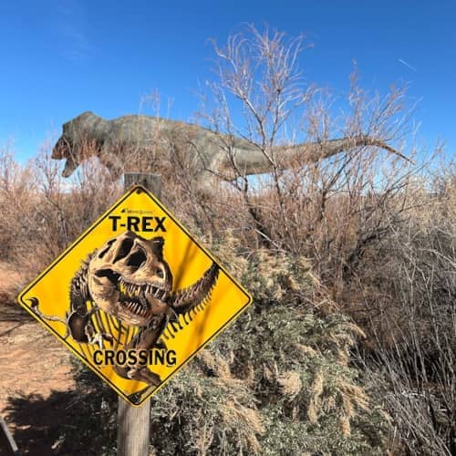 Photo d'une pancarte attention au T-rex avec un T-rex semblant passer derrière